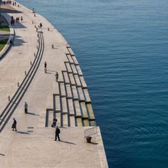 people walking along the edge of a large body of water next to a concrete walkway