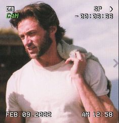 a man with a beard and white t - shirt is holding his jacket over his shoulder