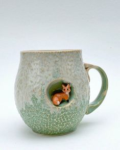 a ceramic cup with a small fox in the hole on it's front side