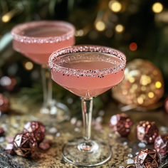 two pink cocktails sitting on top of a table next to christmas ornaments and decorations