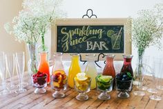 there are many glasses on the table with different drinks in front of it and a chalkboard sign behind them