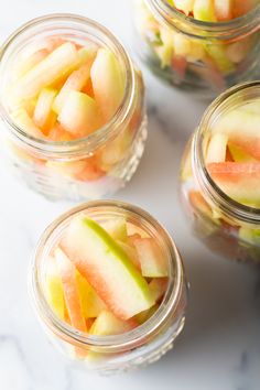 four glass jars filled with sliced fruit on top of a white countertop next to each other