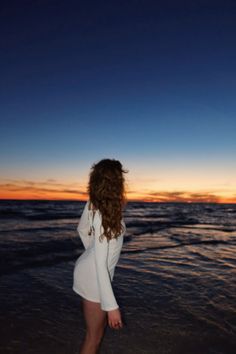 a woman standing on top of a sandy beach next to the ocean at night time