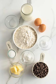 ingredients to make chocolate chip cookies laid out on a marble counter with eggs, butter and flour