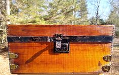 an old wooden box with metal latches in the middle of a wooded area on a sunny day