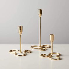 three gold candlesticks and one candle holder on a white table with grey background