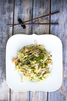 a white plate topped with food next to chopsticks on top of a wooden table