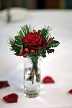 a glass vase filled with red roses and greenery on top of a white table