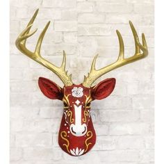 a red and gold deer head mounted on a white brick wall with flowers in the antlers