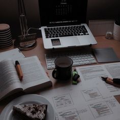 a laptop computer sitting on top of a desk next to an open book and coffee cup