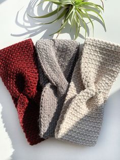 three knitted scarves sitting next to a plant