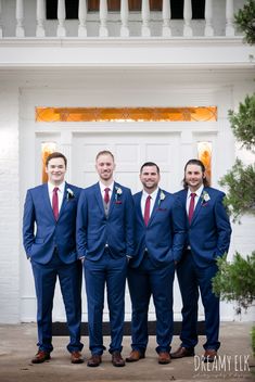 a group of men standing next to each other in front of a white door wearing blue suits and red ties