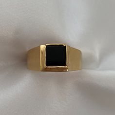 a gold ring with a black stone in the center on a white cloth background,