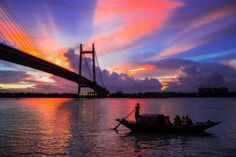 a boat with people in it floating on the water near a bridge at sunset or dawn