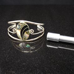 *Description: Beautiful abalone shell oval cuff bracelet in silver tone, nickel silver, from the 1970s. The back of the oval is stamped Alpaca Mexico. This would be a great addition to your vintage jewelry collection or make a great vintage gift! *Approximate Measurements: Length from tip to tip - 5 1/4 Inches with 1 3/4 Inch open, Width - 1 3/8 inches, Oval Shell Center- 1 1/4 Inches by 7/8 Inch *Condition: Great vintage condition. Will see signs of wear under magnification. See photos for deta Silver Oval Cuff Bracelet, Silver Oval Cuff Bracelet With Polished Finish, Vintage Oval Cuff Bracelet With Polished Finish, Oval Cuff Bracelet With Polished Finish, Formal Earrings, Vintage Christmas Gifts, Bracelet In Silver, Book Pieces, Nickel Silver