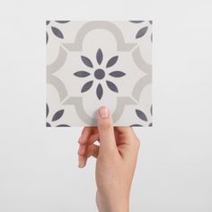 a hand holding up a square tile with black and white designs