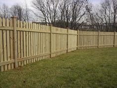 a wooden fence with green grass and trees in the backgroung, behind it is a yellow fire hydrant