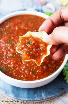 a hand holding a tortilla over a bowl of salsa