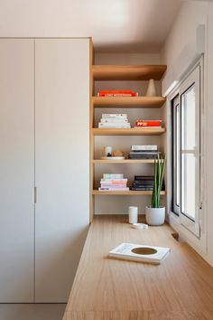 a book shelf in the corner of a room next to a window with books on it