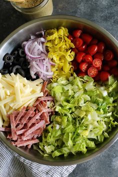 a bowl filled with lettuce, tomatoes, olives and other ingredients next to a jar of mustard