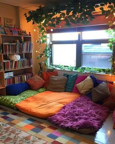 a living room filled with lots of pillows and bookshelves next to a window