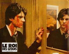 a man with red paint on his face is looking at himself in the mirror