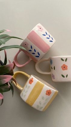 three coffee mugs sitting next to each other on a table with flowers in them