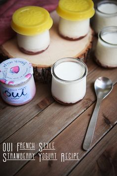 three small jars of yogurt sitting on top of a wooden table next to spoons