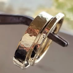 two gold wedding bands sitting on top of each other in front of a glass window