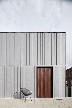 an empty chair sitting in front of a building with metal slats on the side