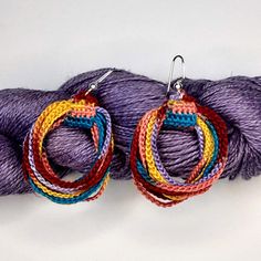 pair of multicolored hoop earrings sitting on purple skeins next to yarn