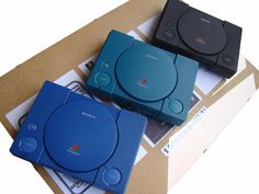 two blue and black playstation consoles sitting next to each other on top of some papers