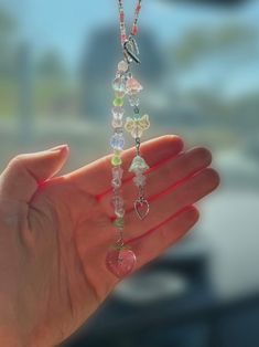 a hand holding a multicolored beaded necklace in front of a car window