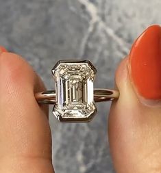 a woman's hand holding an engagement ring with a diamond in the center and a large emerald stone on top