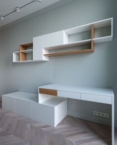 an empty room with white furniture and wooden shelves on the wall, along with herringbone flooring