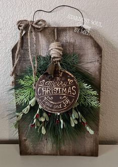 a christmas sign hanging from the side of a wooden plaque with holly and pine cones