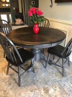 a wooden table with four chairs around it and a vase filled with flowers on top