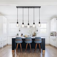 a kitchen with wooden floors and white walls, lights hanging from the ceiling over the island