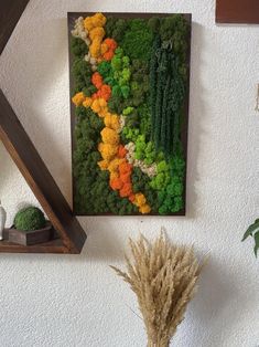 an arrangement of vegetables is displayed on the wall next to a vase with dried grass in it