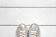 a person's silver sneakers with white laces on them sitting on a wooden floor