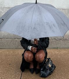 a woman is sitting on the sidewalk with an umbrella over her head and holding a purse