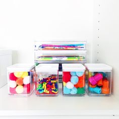 plastic containers filled with different types of colored balls and pencils on top of a white table