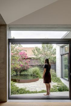 a woman standing in front of a glass door looking out onto a garden and pond