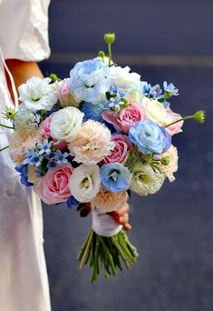 a bride holding a bouquet of white and blue flowers in her hand on the street