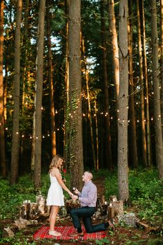 a man kneeling down next to a woman on a red rug in the middle of a forest