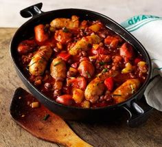 a skillet filled with meat and vegetables on top of a wooden table next to a napkin