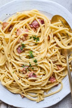 a plate of pasta with ham and parmesan cheese on top, next to a fork