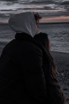 two people sitting on the beach watching the sunset