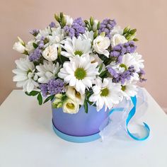 a bouquet of white and purple flowers sitting in a blue vase with a ribbon around it