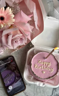 a pink birthday cake in a box next to a cell phone with the message happy birthday written on it